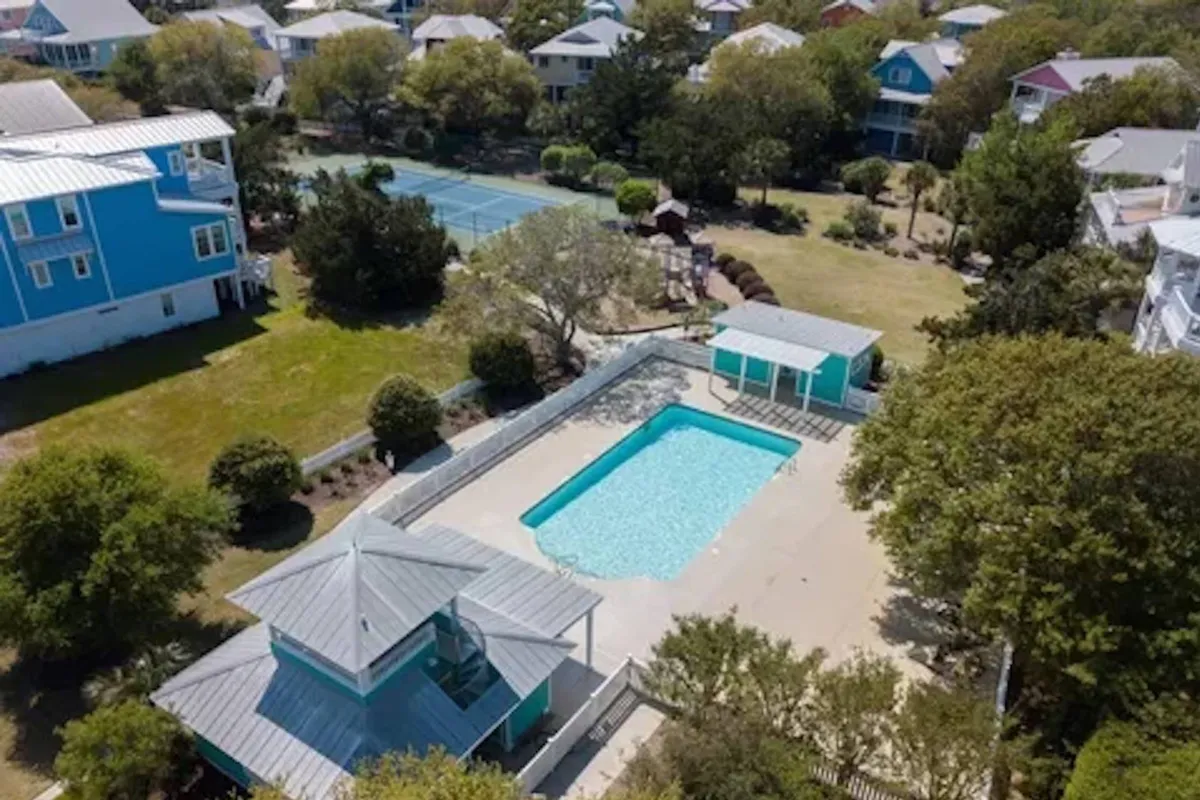This image features a vibrant outdoor recreation area with a swimming pool, tennis court, and outdoor cabana, all surrounded by lush greenery. The setting is lively and inviting, ideal for active gatherings and relaxing afternoons.