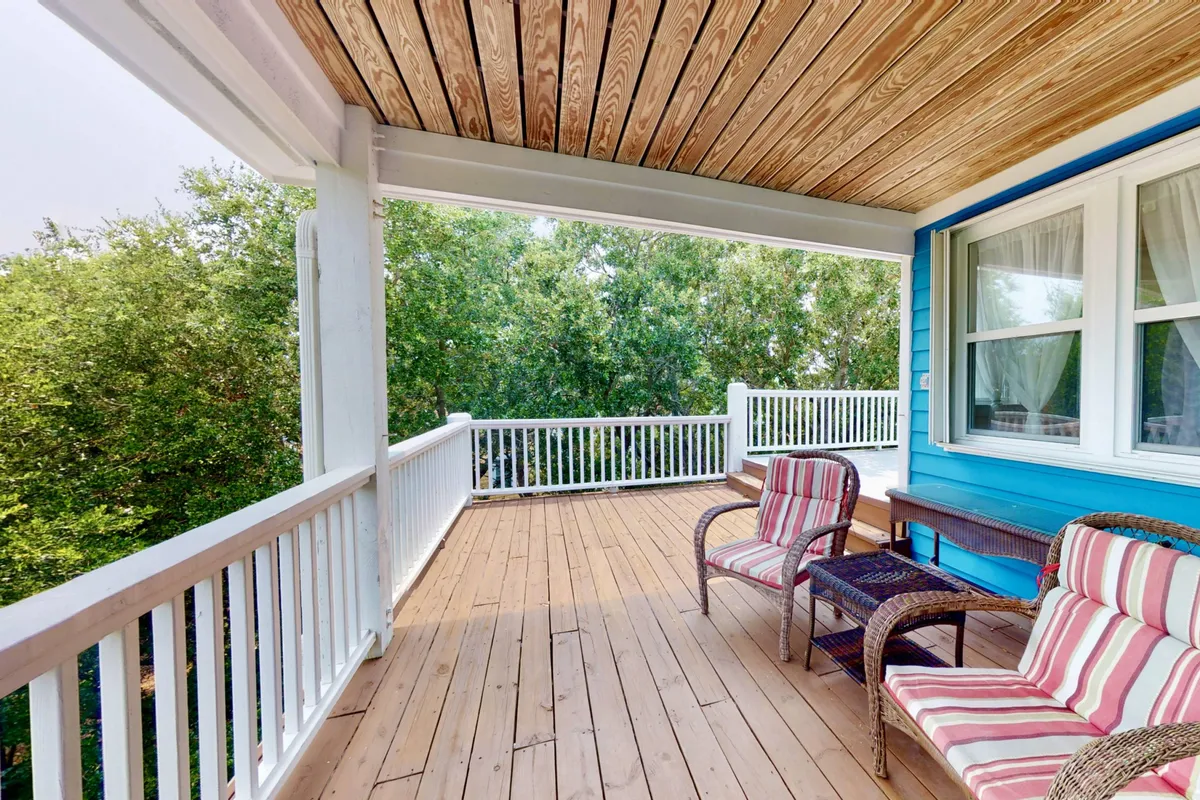 A tranquil wooden deck furnished with striped chairs, enveloped by lush green foliage. The setting is perfect for relaxing, enjoying a morning coffee, or hosting a quiet gathering, with a sense of privacy and comfort.