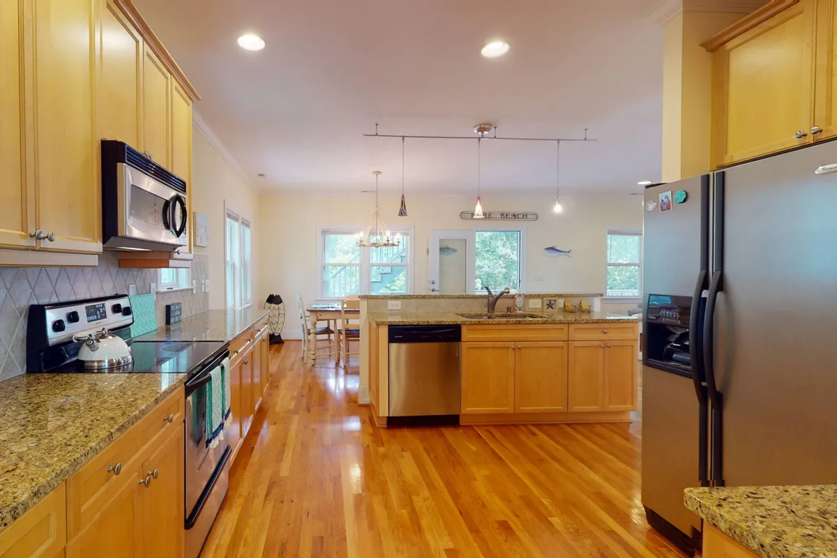 A bright, cheerful kitchen with granite countertops, stainless steel appliances, wooden flooring, a kitchen island with bar seating, and an adjacent dining area. The setup encourages both cooking and socializing, making it ideal for family time and entertaining guests.