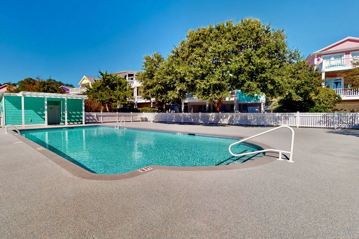 An exterior view of a swimming pool surrounded by lush greenery and a poolside lounge area. The scene suggests relaxation, swimming, sunbathing, and friendly gatherings, all in a tranquil, resort-style setting.