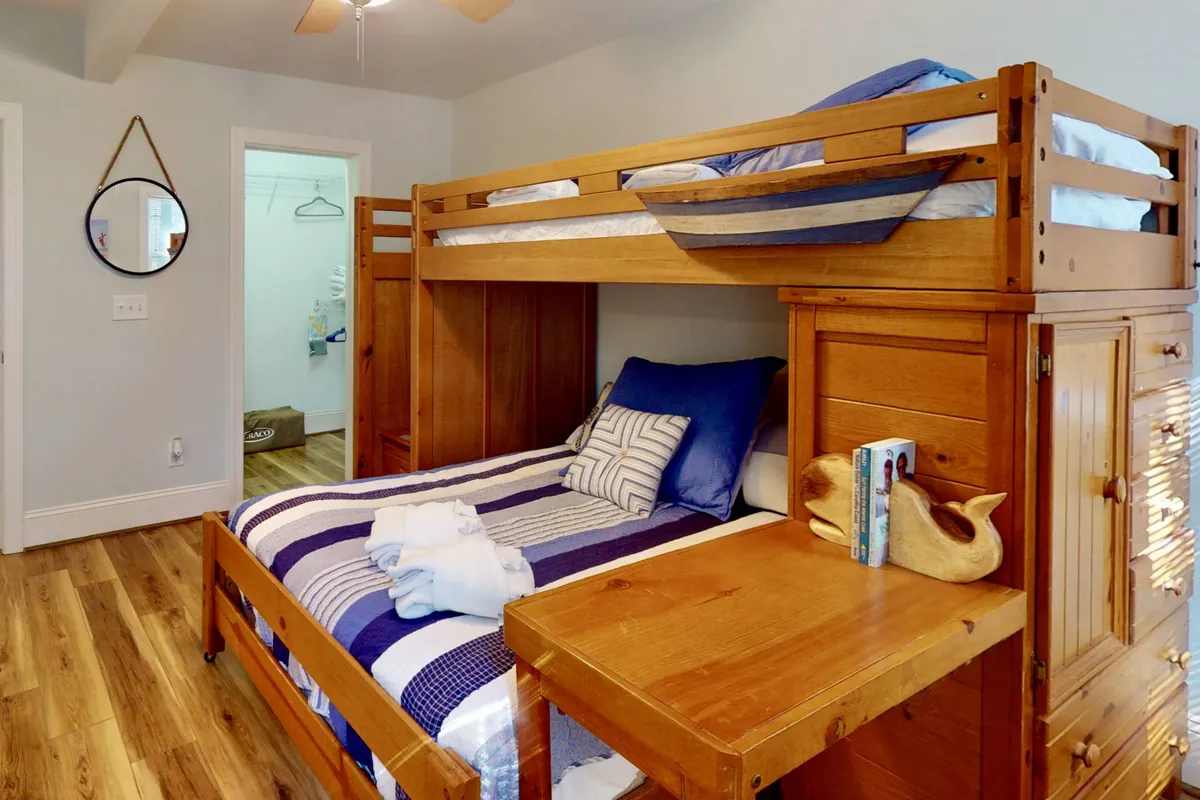 A cozy kids' room with a bunk bed featuring striped bedding, a wooden desk, and a decorative bird figurine. The space is cheerful and practical, ideal for families with children, and hints at thoughtful touches that make young guests feel at home.