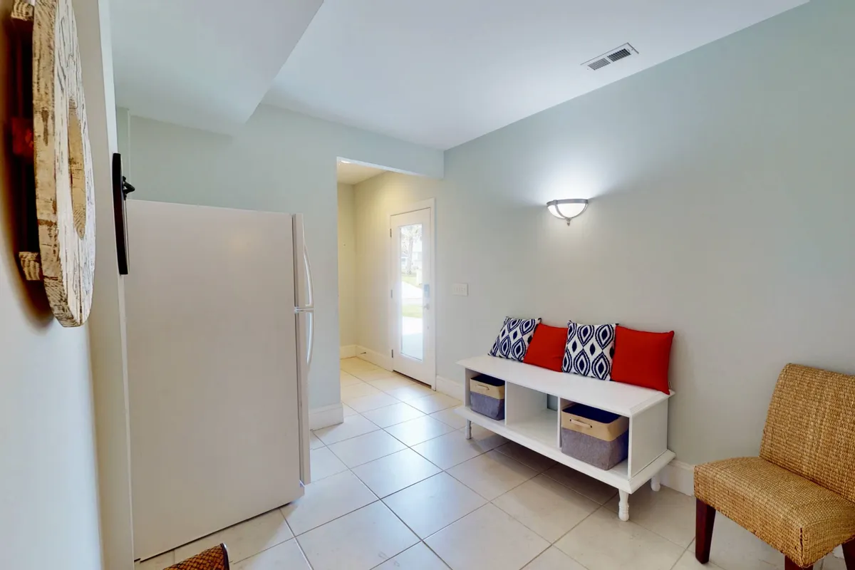 A welcoming entryway with a comfortable seating area, decorative pillows, a light fixture, and a refrigerator visible in the background. The arrangement feels homey and suggests a pet-friendly, accessible environment where guests and their furry companions are immediately at ease.