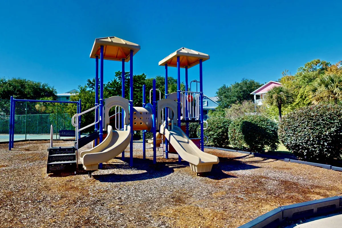 A lively playground featuring sturdy slides and climbing structures surrounded by lush greenery and a safety surface, inviting families and children to play, socialize, and enjoy outdoor fun together.