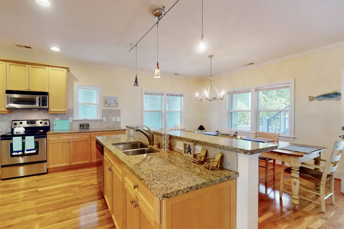 A modern kitchen and dining area, highlighted by granite countertops, stainless steel appliances, a wooden dining table, and elegant overhead lighting. The space is warm and functional, facilitating both cooking and entertaining, with enough room for family meals or friendly gatherings.