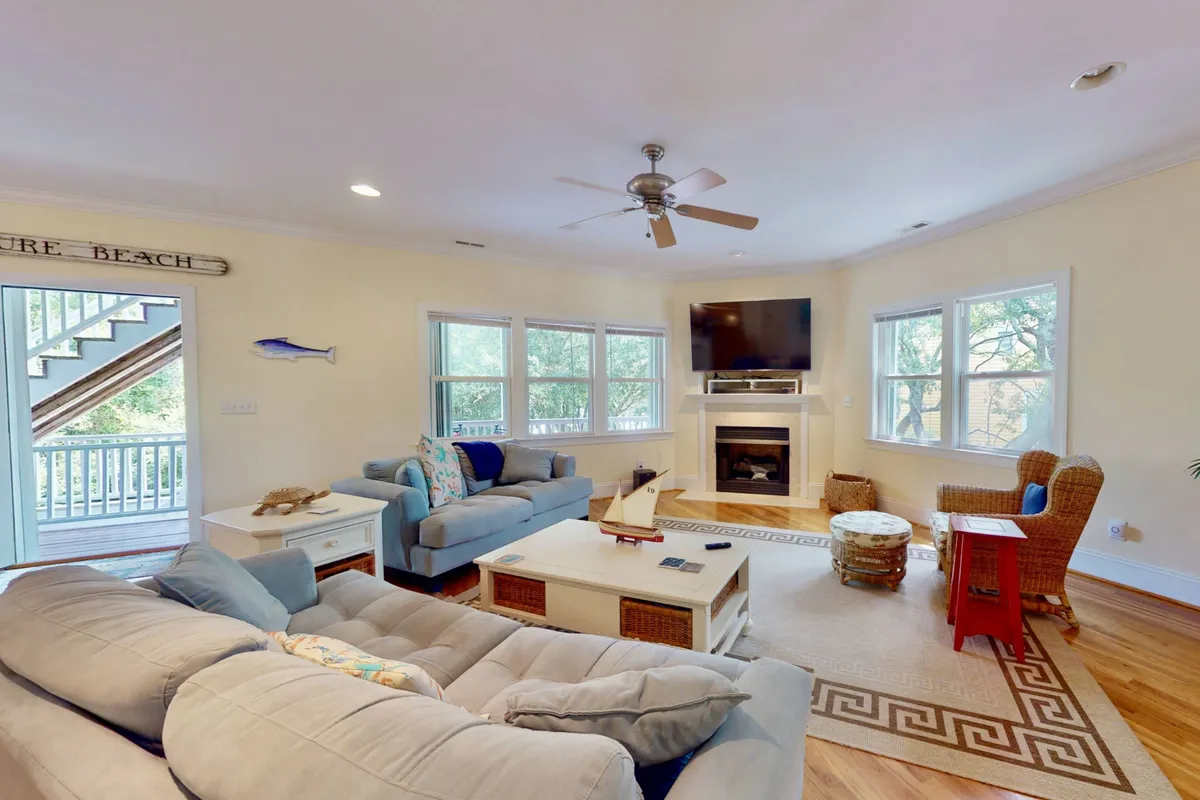 A cozy family room with a plush sofa adorned with decorative pillows, a fireplace, TV, coffee table, and direct access to an outdoor staircase. The room is bathed in natural light and arranged to foster relaxation, games, and social interaction.