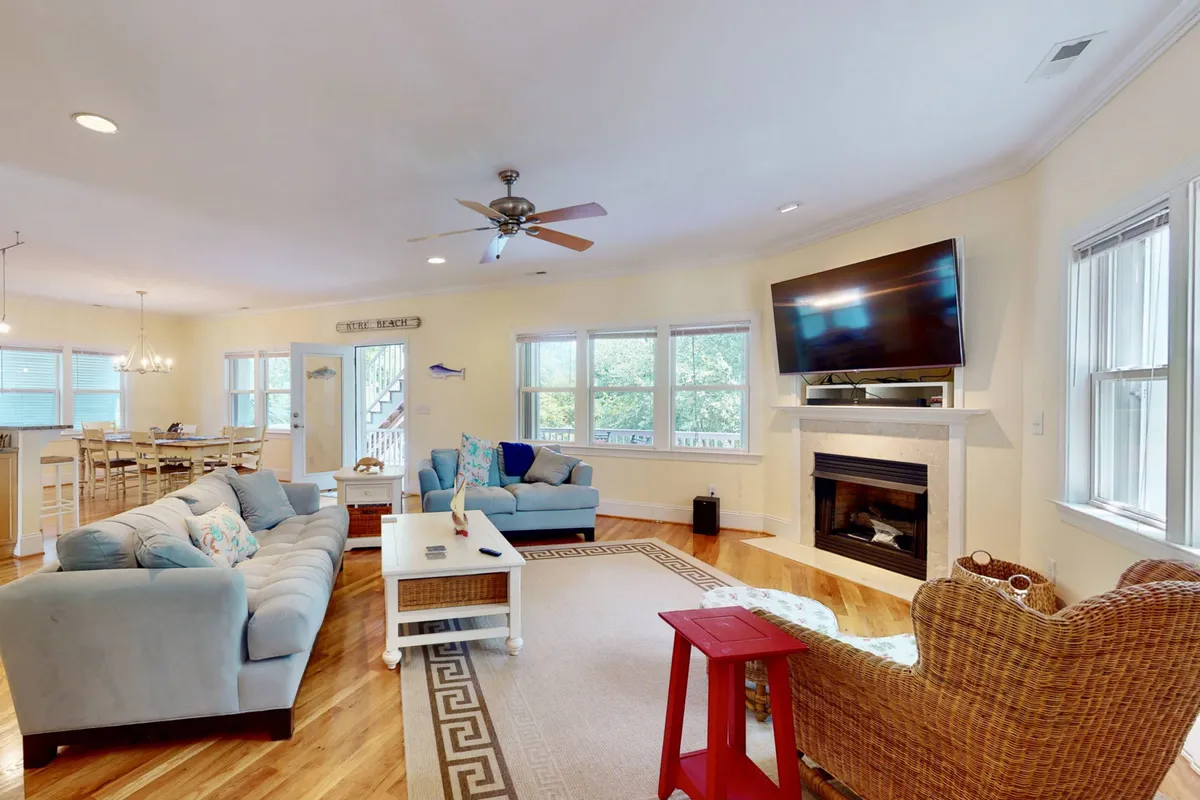 A spacious and inviting family room featuring comfortable sofas, a fireplace, a TV, a decorative table, and a woven armchair. The setup is designed for gatherings, with ample seating for multiple people and a relaxed, friendly atmosphere perfect for movie nights, board games, or quiet chats.