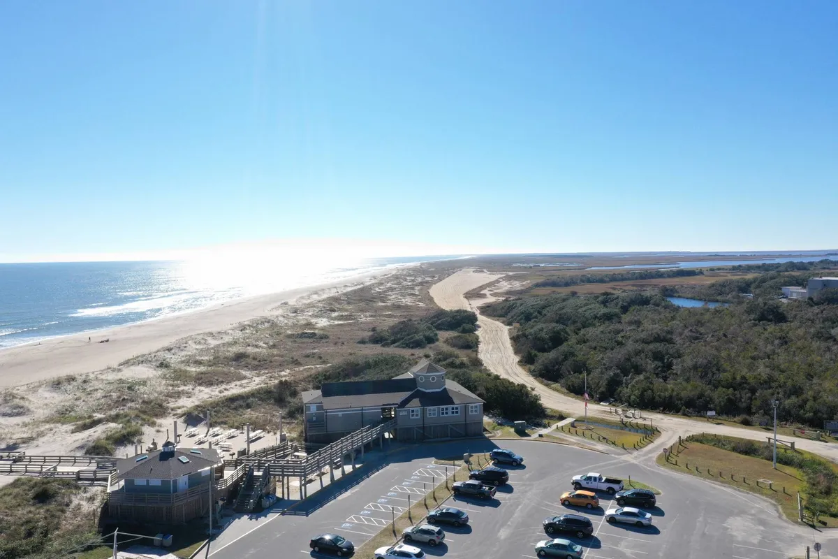 A sweeping view of the expansive beach with clear ocean vistas, a convenient parking area, and a boardwalk structure leading towards the shore. The image radiates a sense of relaxation and outdoor enjoyment, capturing key elements of the coastal lifestyle.